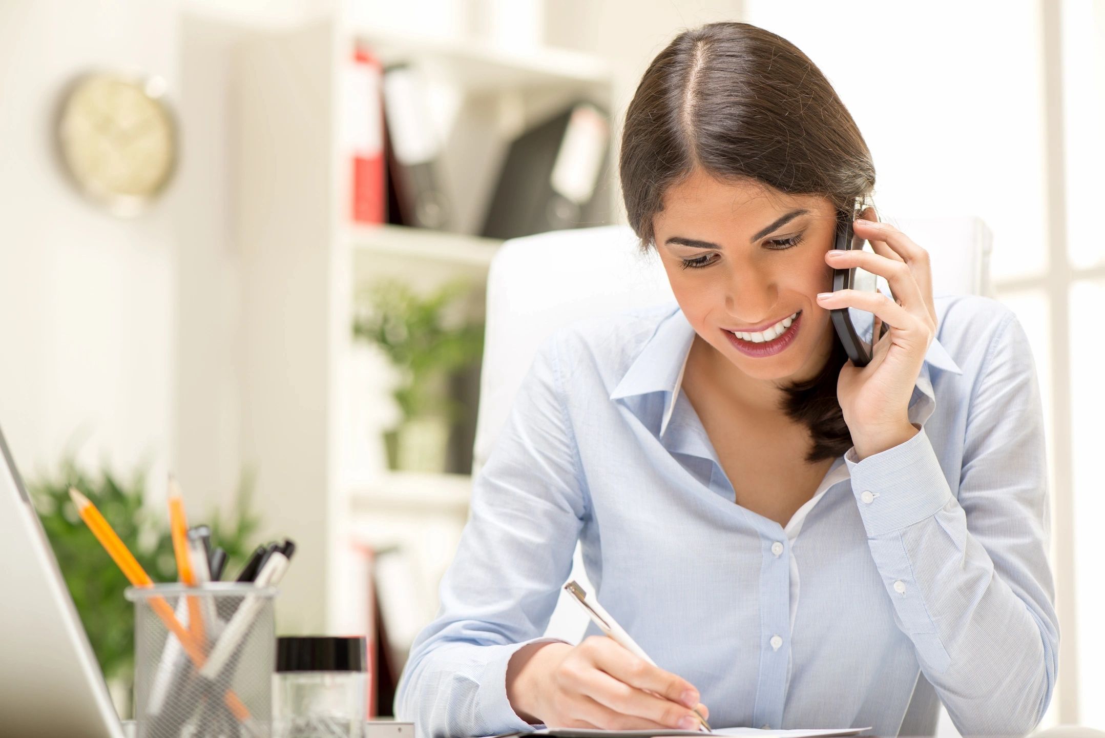 Professional woman speaking on the phone and taking notes at her desk